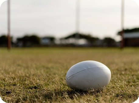 Bola de râguebi colocada num campo de relva antes de um jogo desportivo ao ar livre.